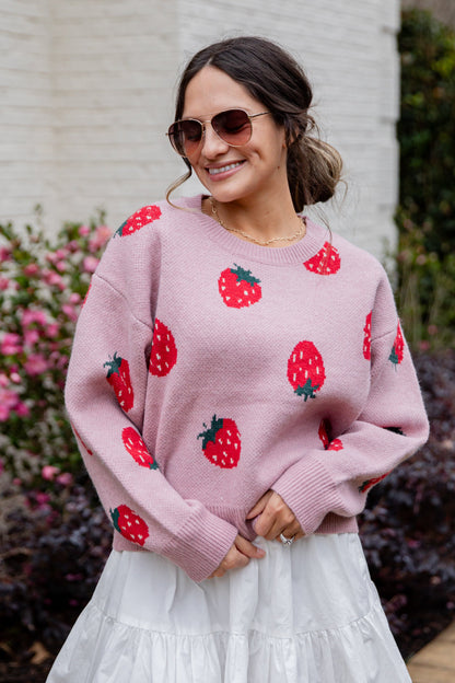 Woman wearing a pink sweater with strawberry patterns outdoors.