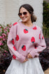 Woman wearing a pink sweater with strawberry patterns outdoors.