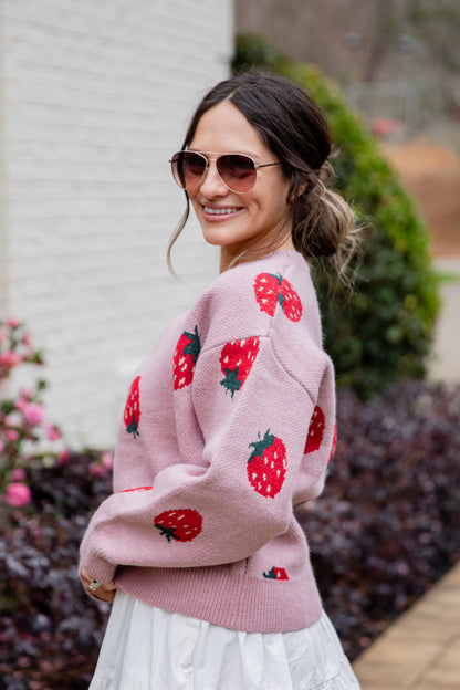 Woman wearing a pink sweater with strawberry patterns outdoors.