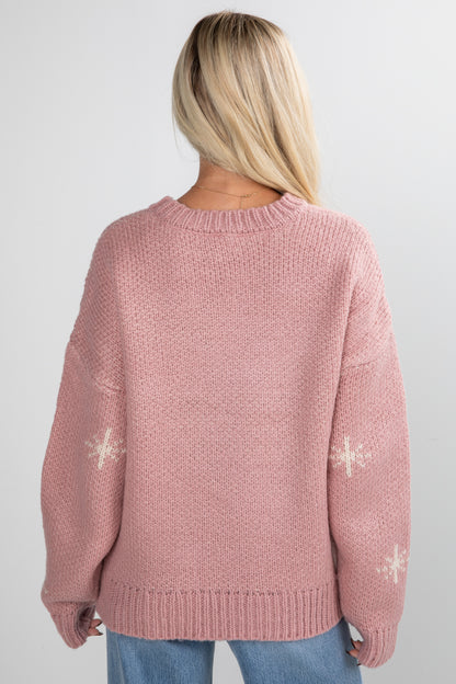 Pink knitted sweater with snowflake patterns worn by a person on a white background