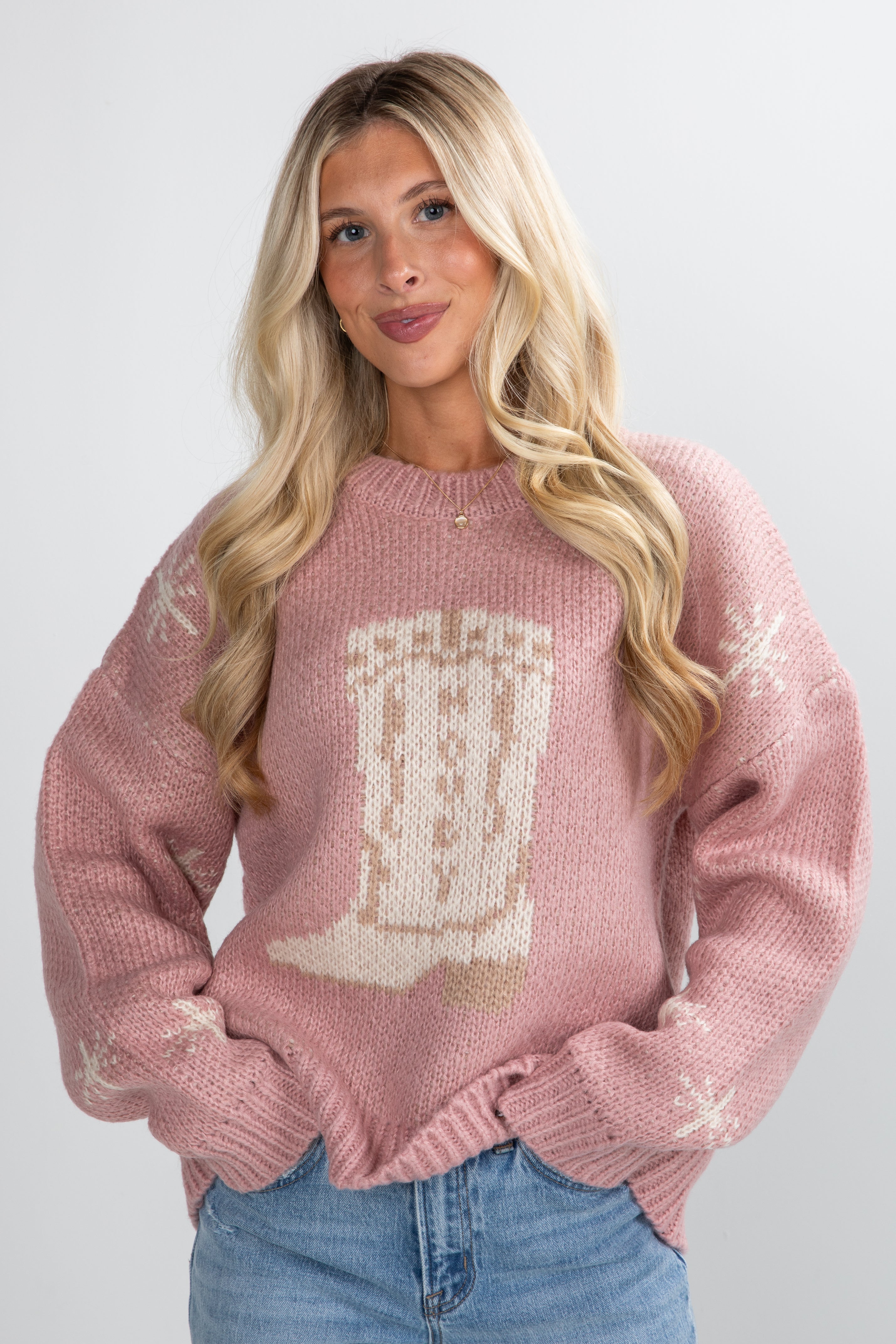 Woman wearing a pink sweater with a graphic design on a plain background