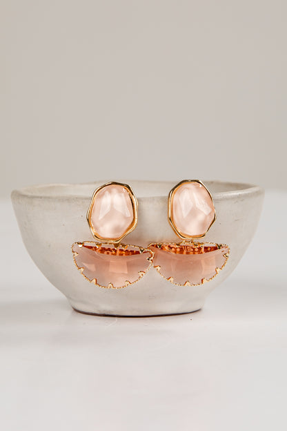 Rose gold earrings with pink stones in a white bowl on a light gray background