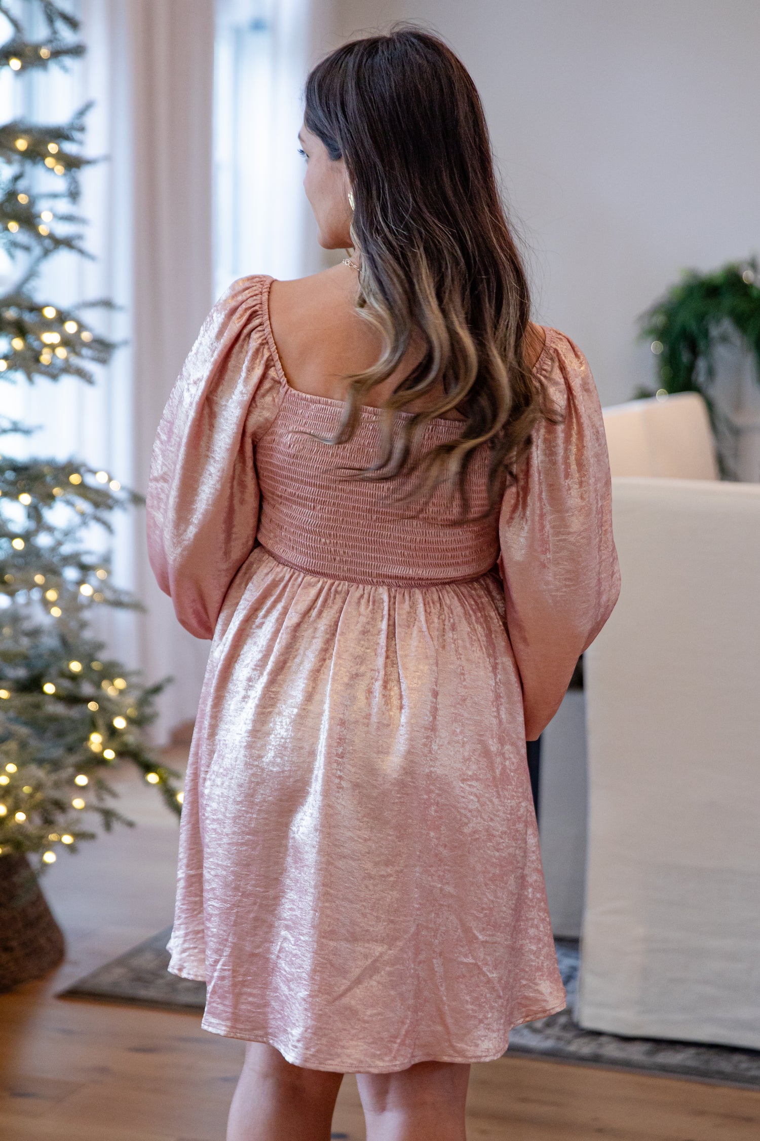 Woman in a pink dress standing in a room with a Christmas tree in the background