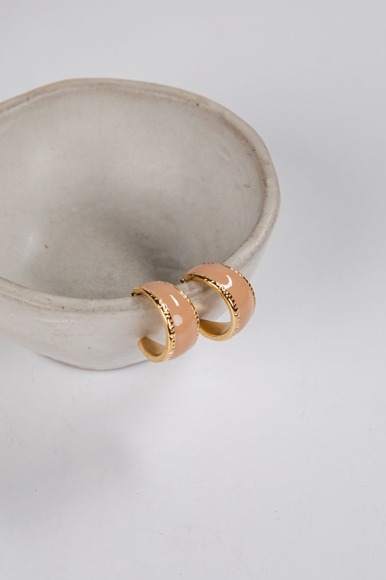 Gold hoop earrings on a white ceramic bowl