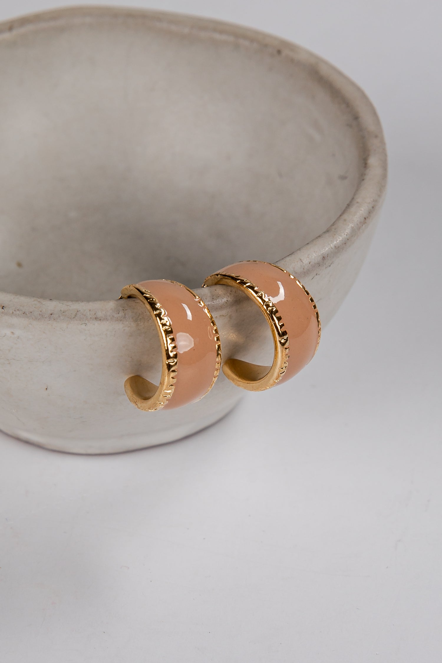 Pair of peach-colored hoop earrings with gold accents on a light gray background