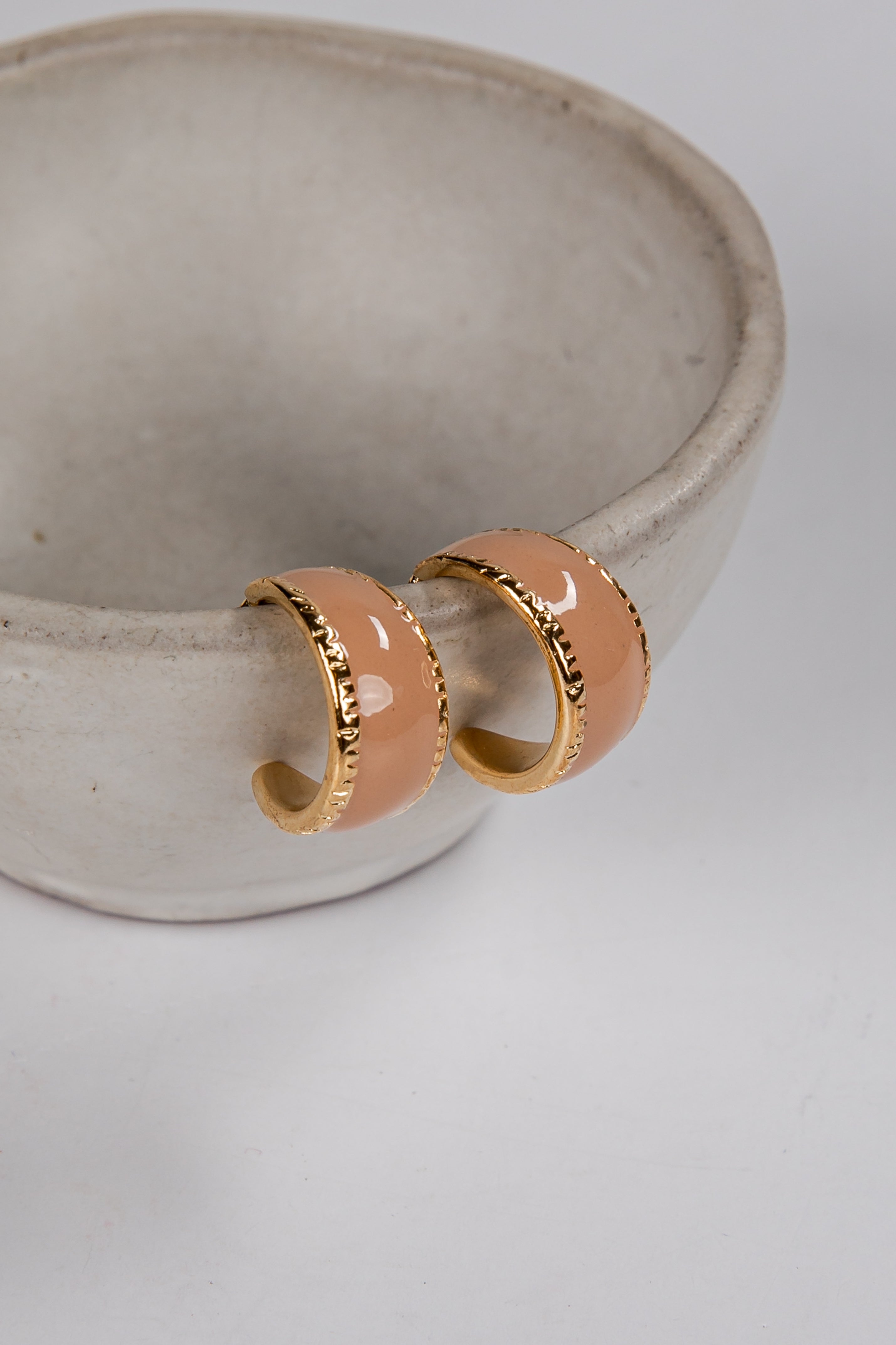 Pair of peach-colored hoop earrings with gold accents on a light gray background