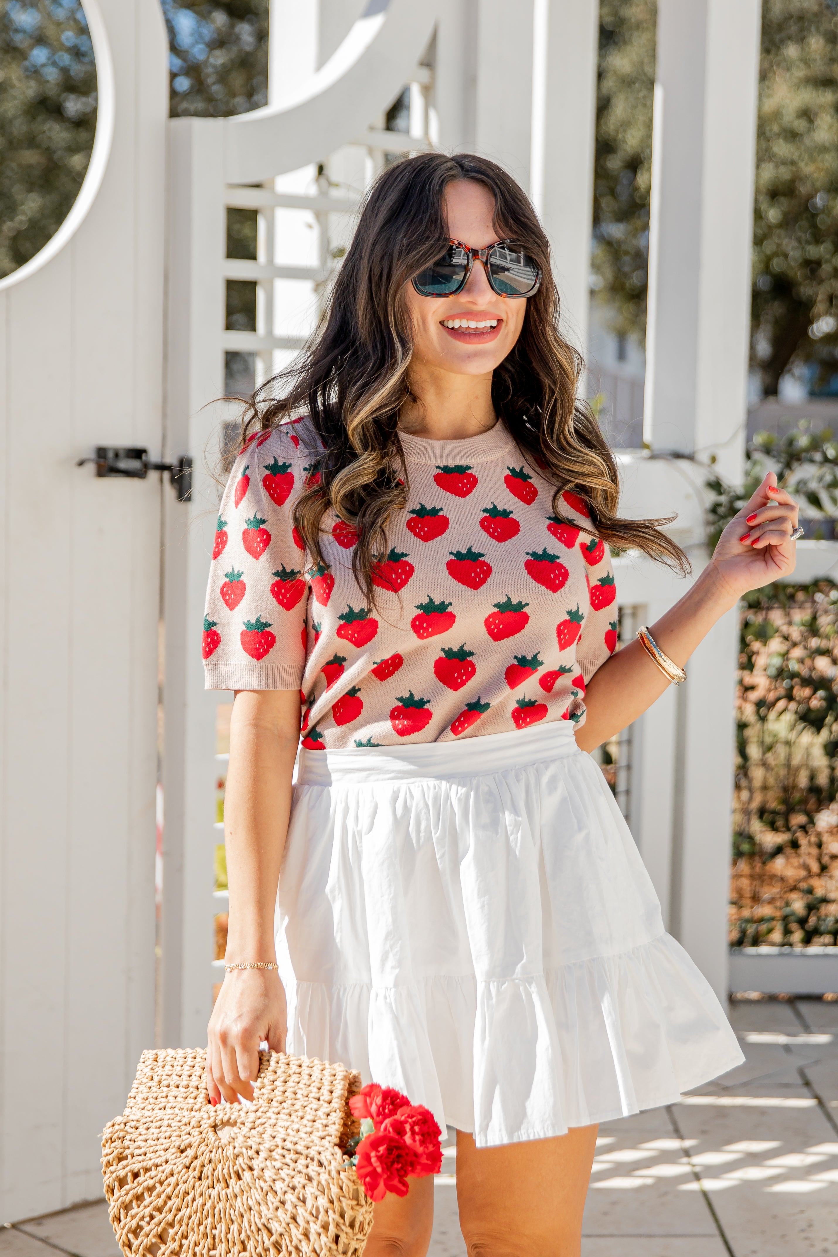 Woman wearing a strawberry-patterned top and white skirt outdoors.