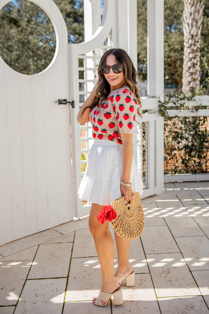 Woman in a red floral top and white skirt standing in front of a white gate.