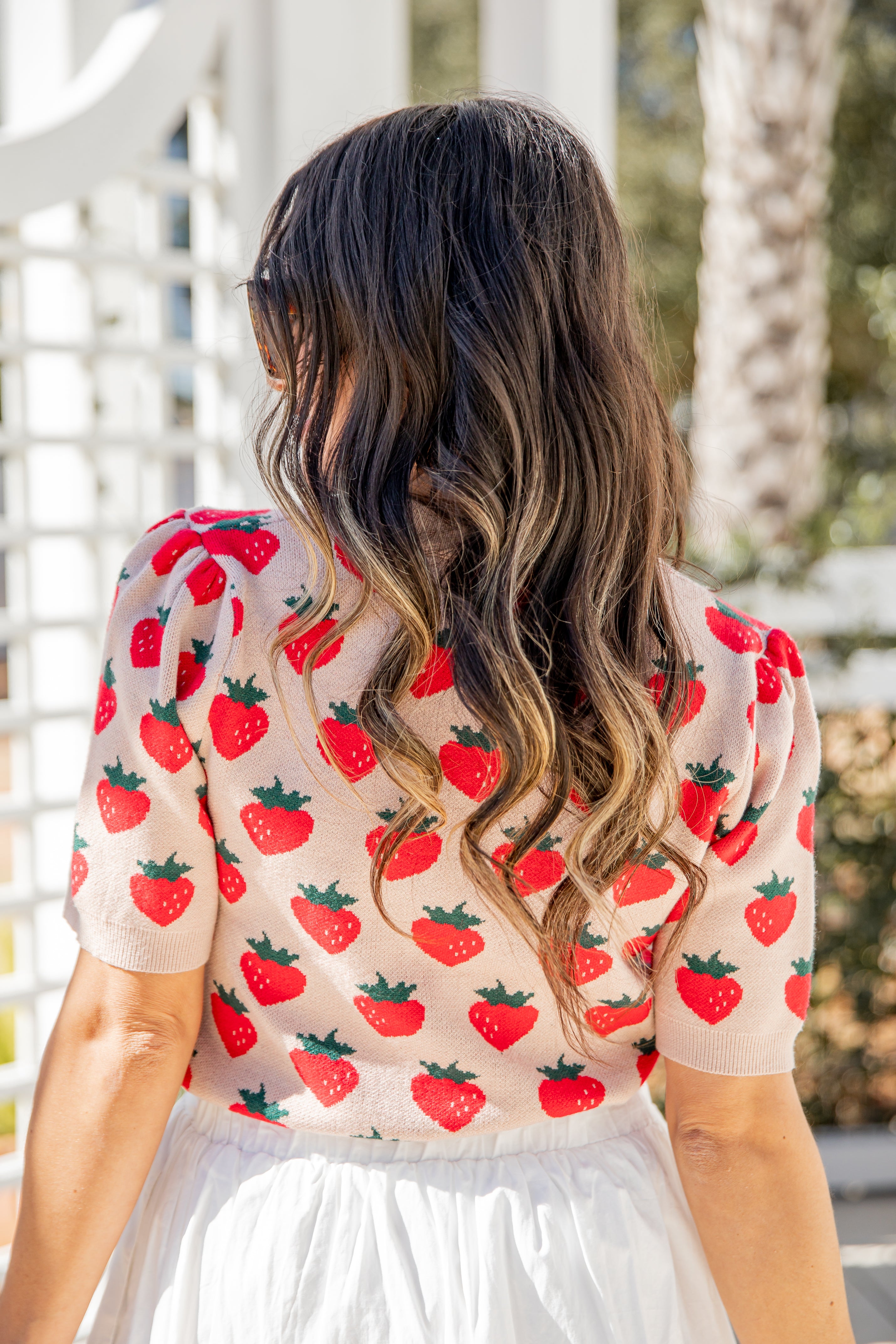 Woman wearing a strawberry patterned top with a blurred outdoor background