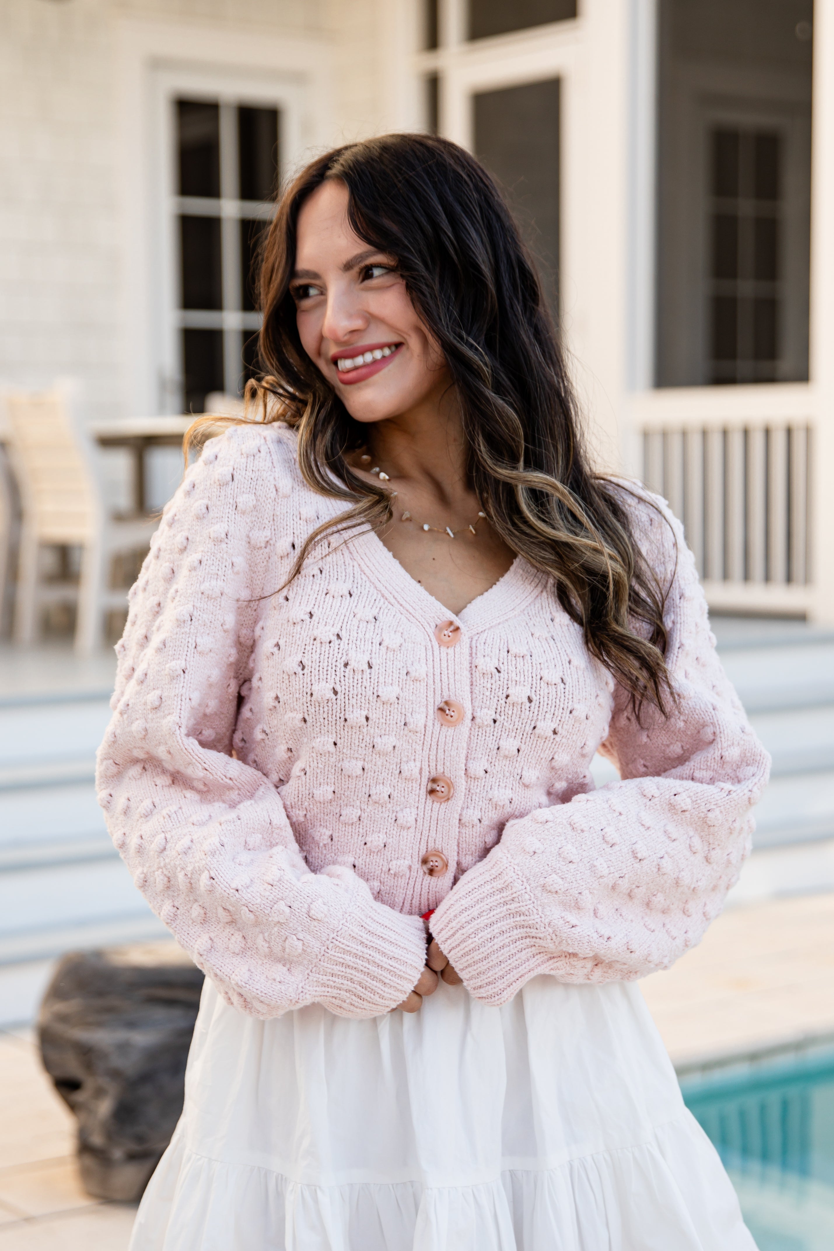 Woman in a pink sweater and white skirt standing by a poolside.