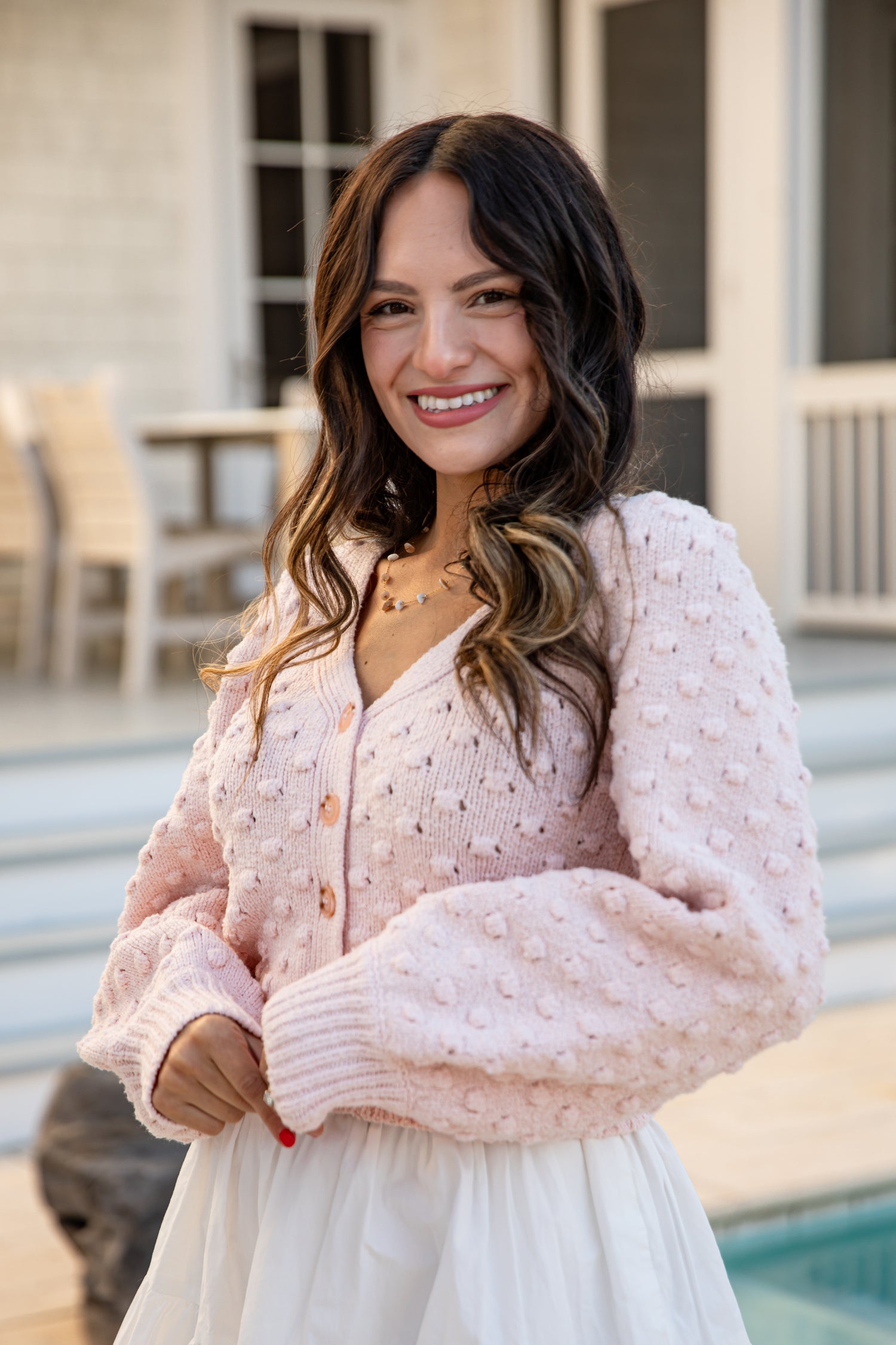 Woman wearing a light pink cardigan with a blurred outdoor background