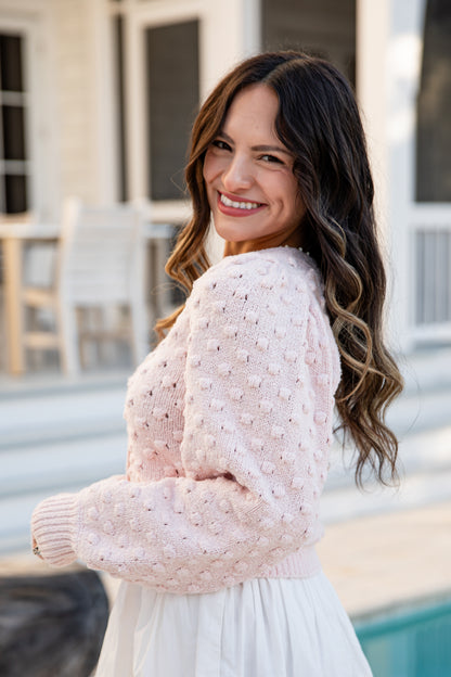 Woman in a pink sweater and white skirt standing by a poolside.