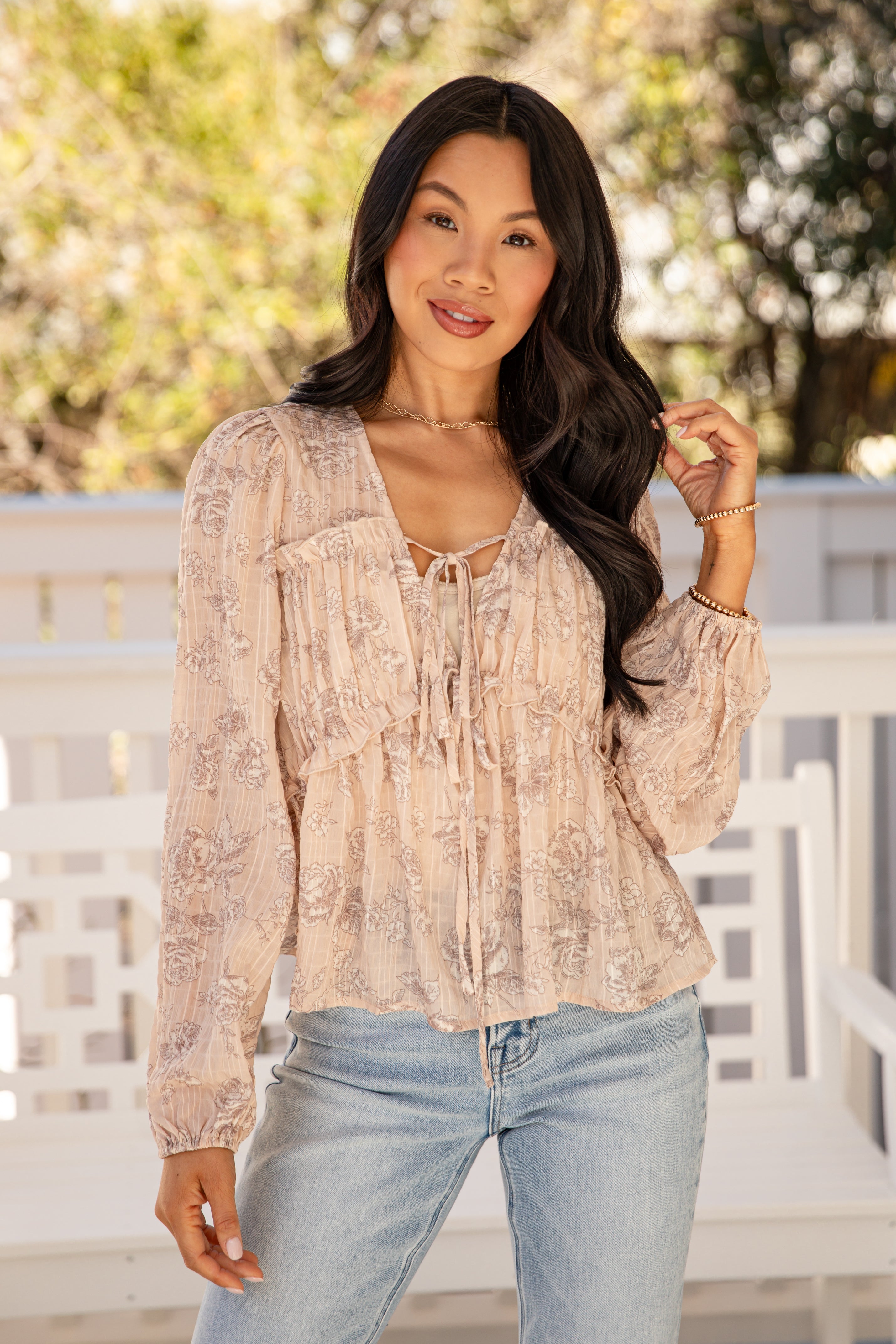Woman wearing a beige patterned blouse and light blue jeans outdoors.