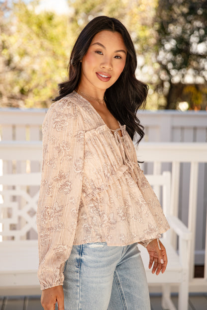 Woman wearing a beige lace top and jeans on a blurred outdoor background