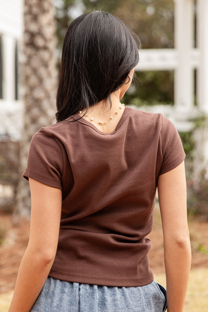Person wearing a brown t-shirt with a blurred outdoor background