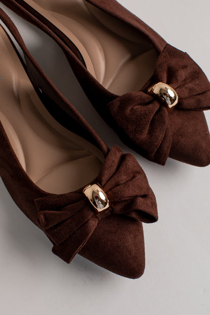 A pair of dark brown suede pointed-toe flats with decorative bows and shiny gold metal accents, shown on a neutral light gray background.
