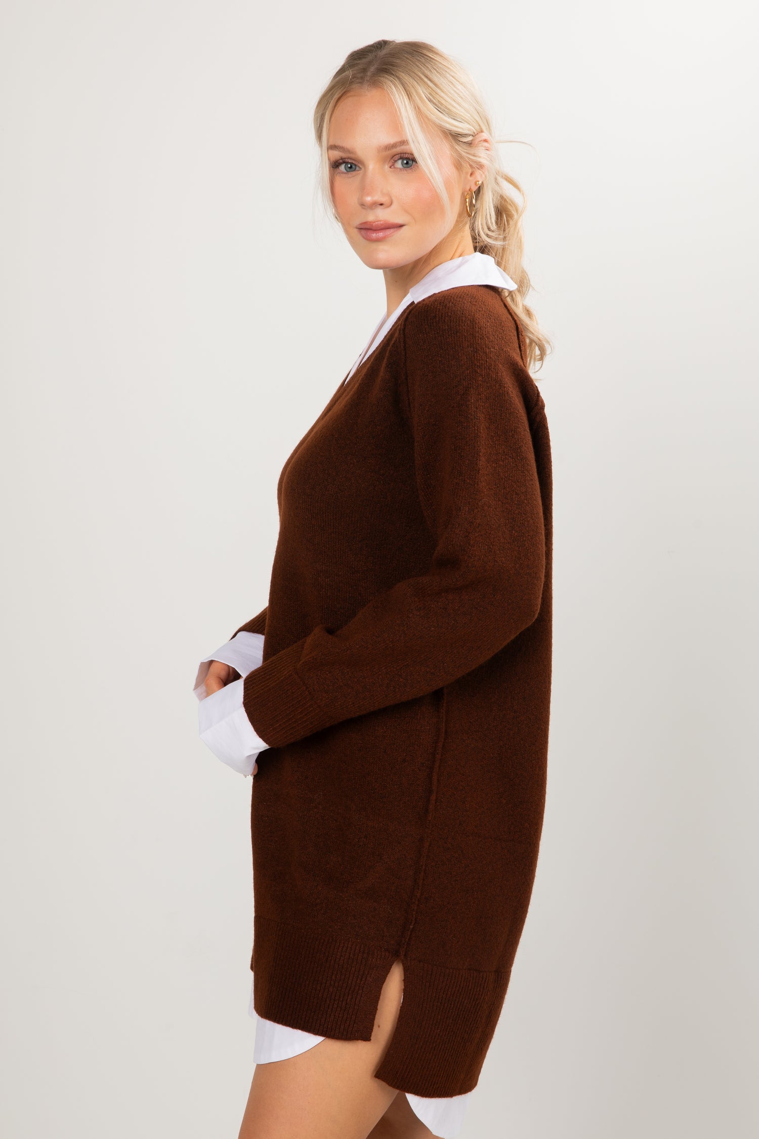 Woman wearing a brown V-neck sweater dress layered with white collared shirt.