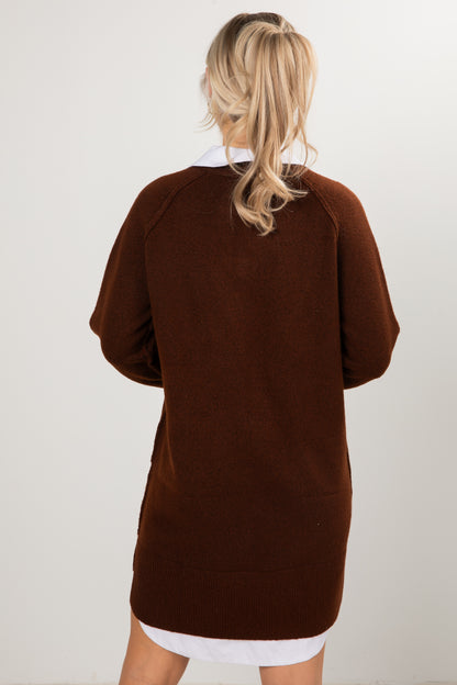 Woman wearing a brown V-neck sweater dress layered with white collared shirt.