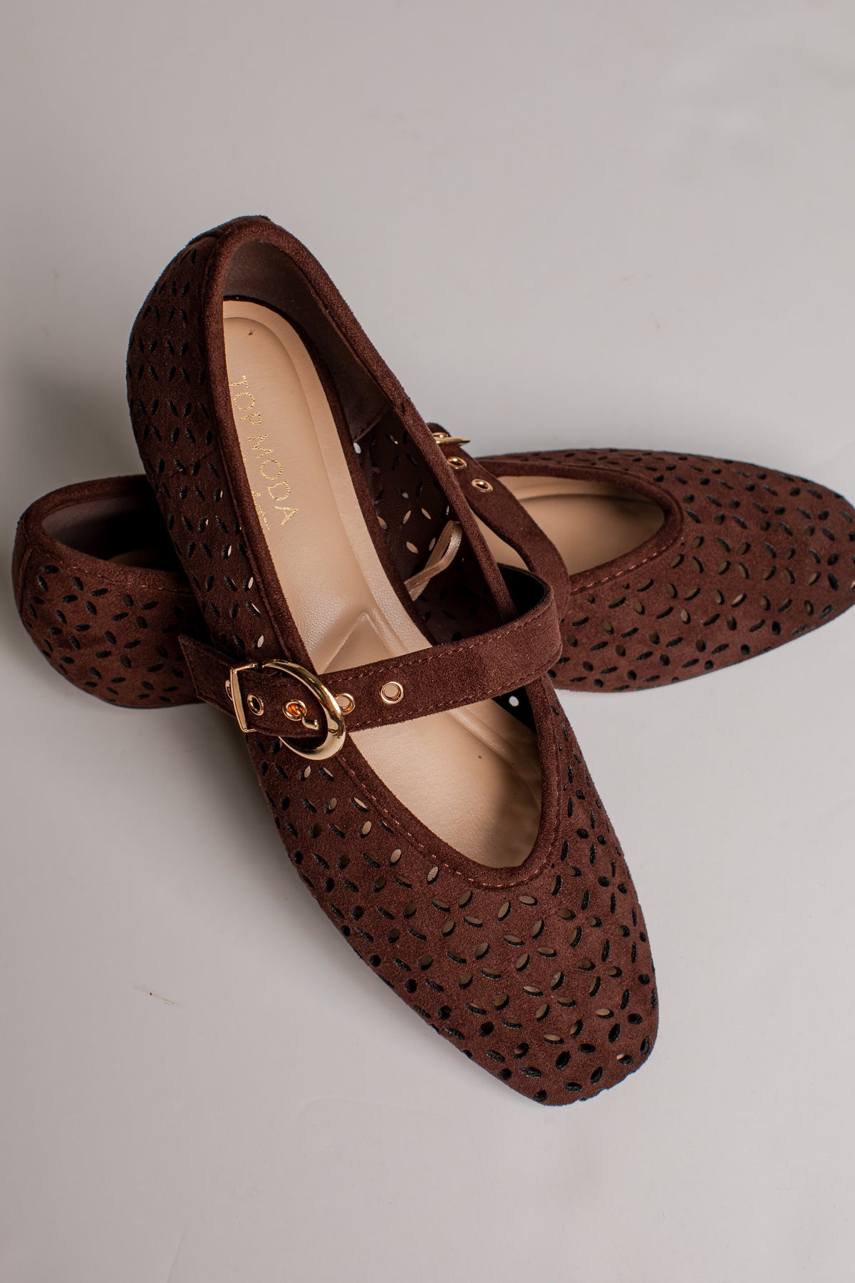 A pair of dark brown Mary Jane shoes with a textured, perforated upper and a gold-tone buckle strap, displayed on a light gray background.
