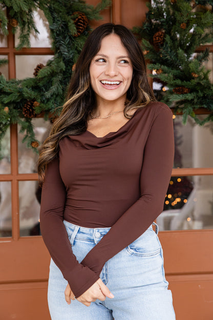 Woman wearing a brown long-sleeve top and light blue jeans standing in front of a decorated Christmas tree.