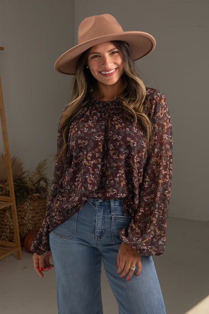 Woman wearing a floral blouse, jeans, and a wide-brimmed hat indoors.
