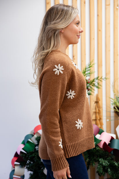 Woman wearing a brown sweater with white flower patterns in a festive setting.