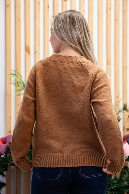 Person wearing a brown sweater standing in front of a wooden fence.