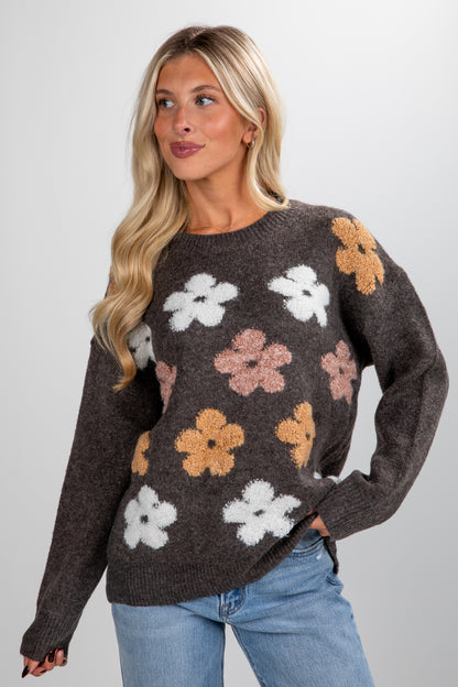 Woman wearing a dark brown sweater with floral patterns on a plain background
