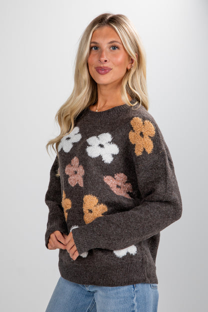 Woman wearing a brown sweater with floral patterns on a plain background