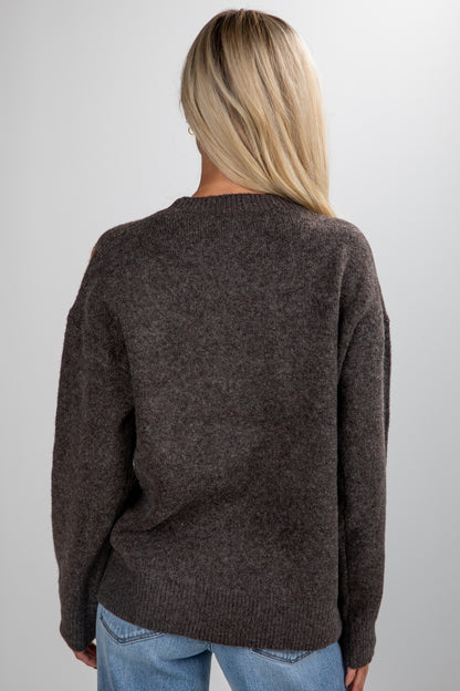 Person wearing a brown sweater and blue jeans on a plain background