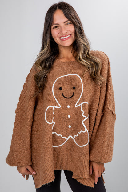 Woman wearing a brown sweater with a gingerbread man design on a plain background