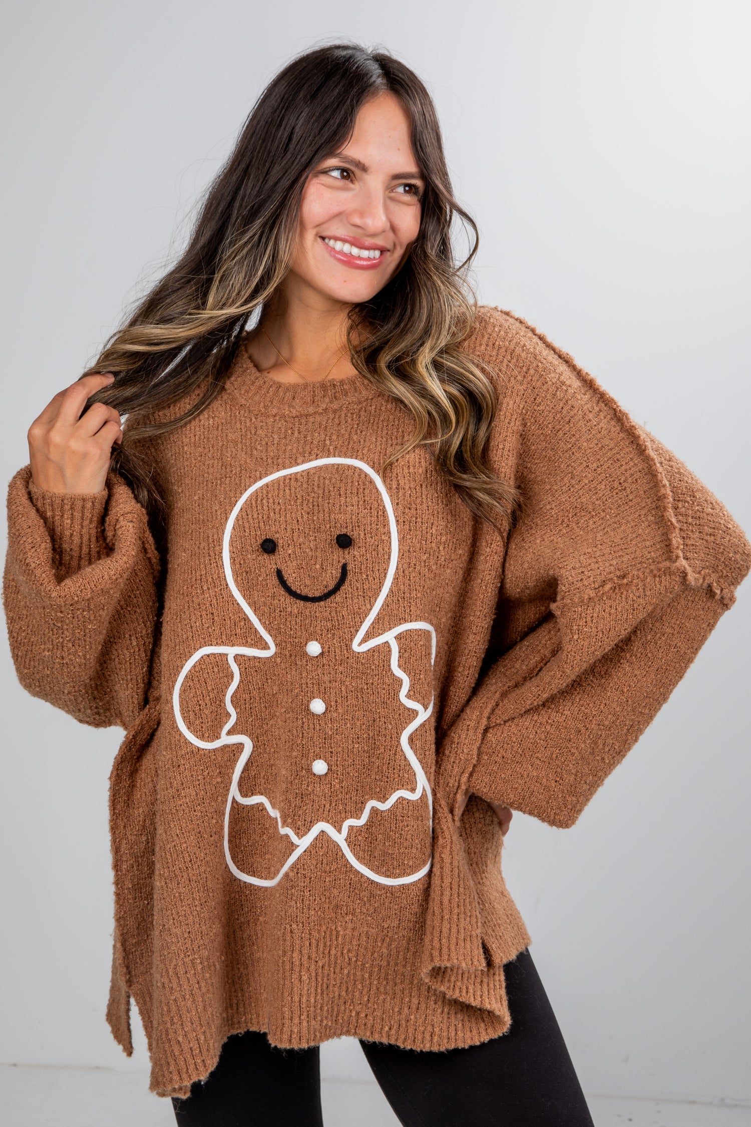 Woman wearing a brown sweater with a gingerbread man design against a white background