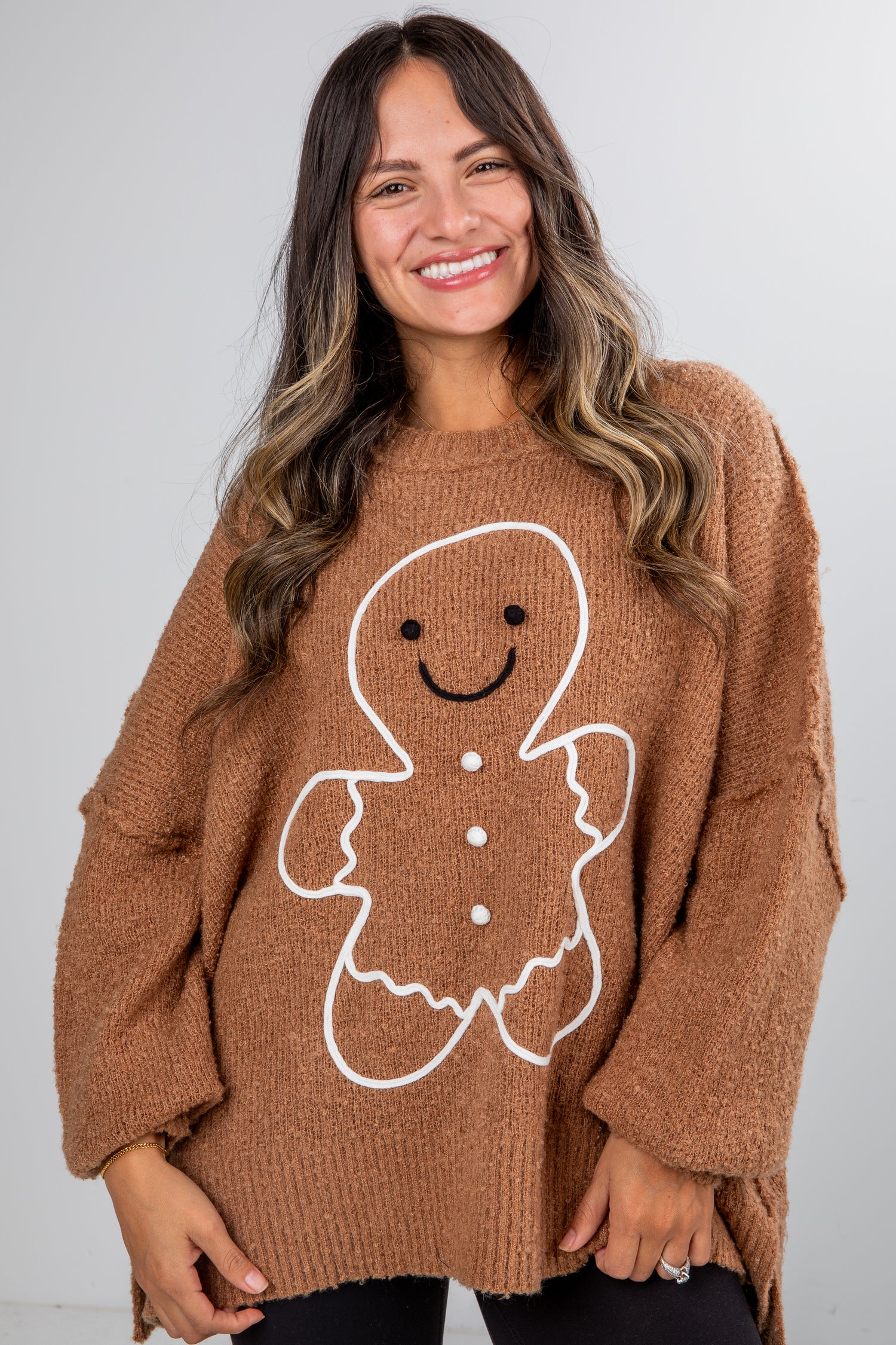 Woman wearing a brown sweater with a gingerbread man design against a white background
