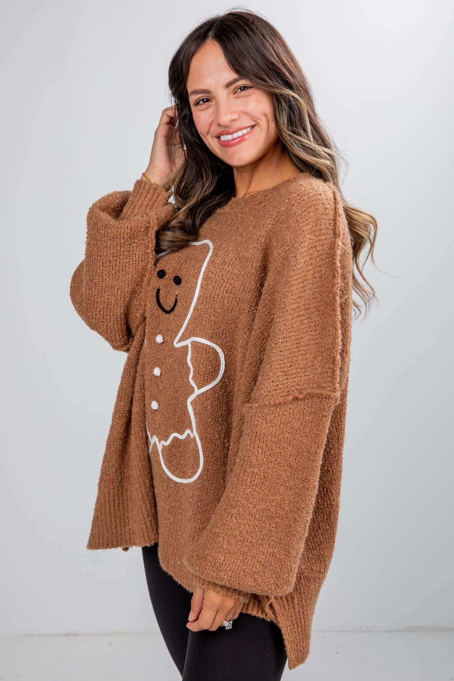 Woman wearing a brown sweater with a gingerbread man design on a white background