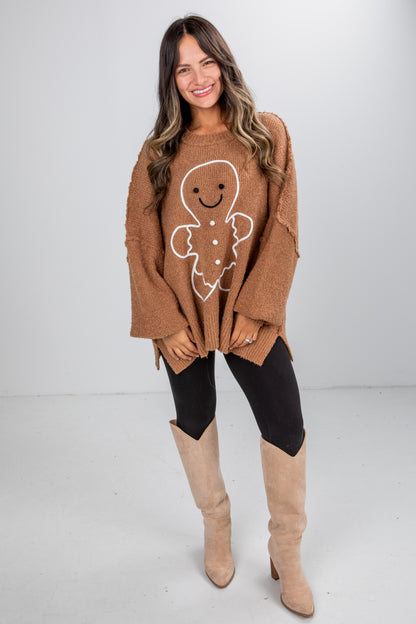 Woman wearing a brown sweater with a gingerbread man design and beige knee-high boots on a white background