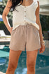 Woman wearing a white crochet top and checkered shorts by a pool.