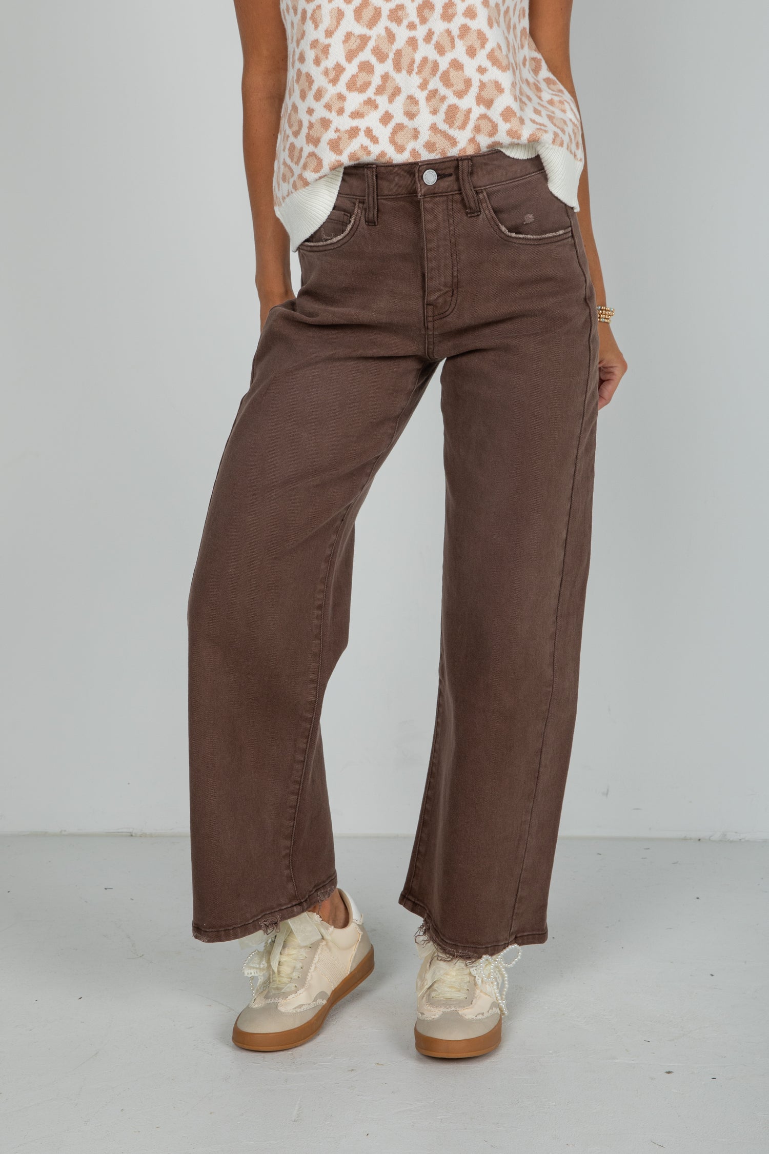 Person wearing brown wide-leg pants and a leopard print top on a white background