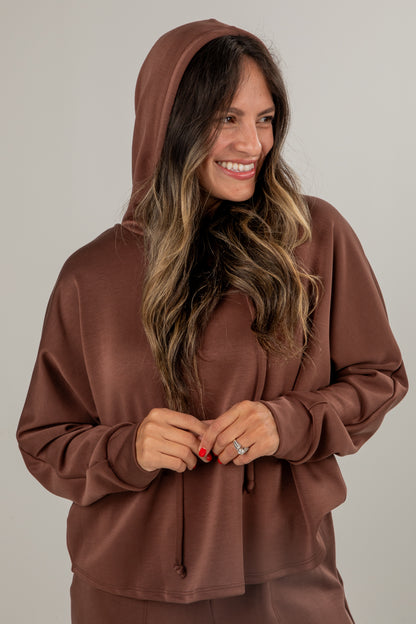 Woman wearing a brown hoodie against a plain background