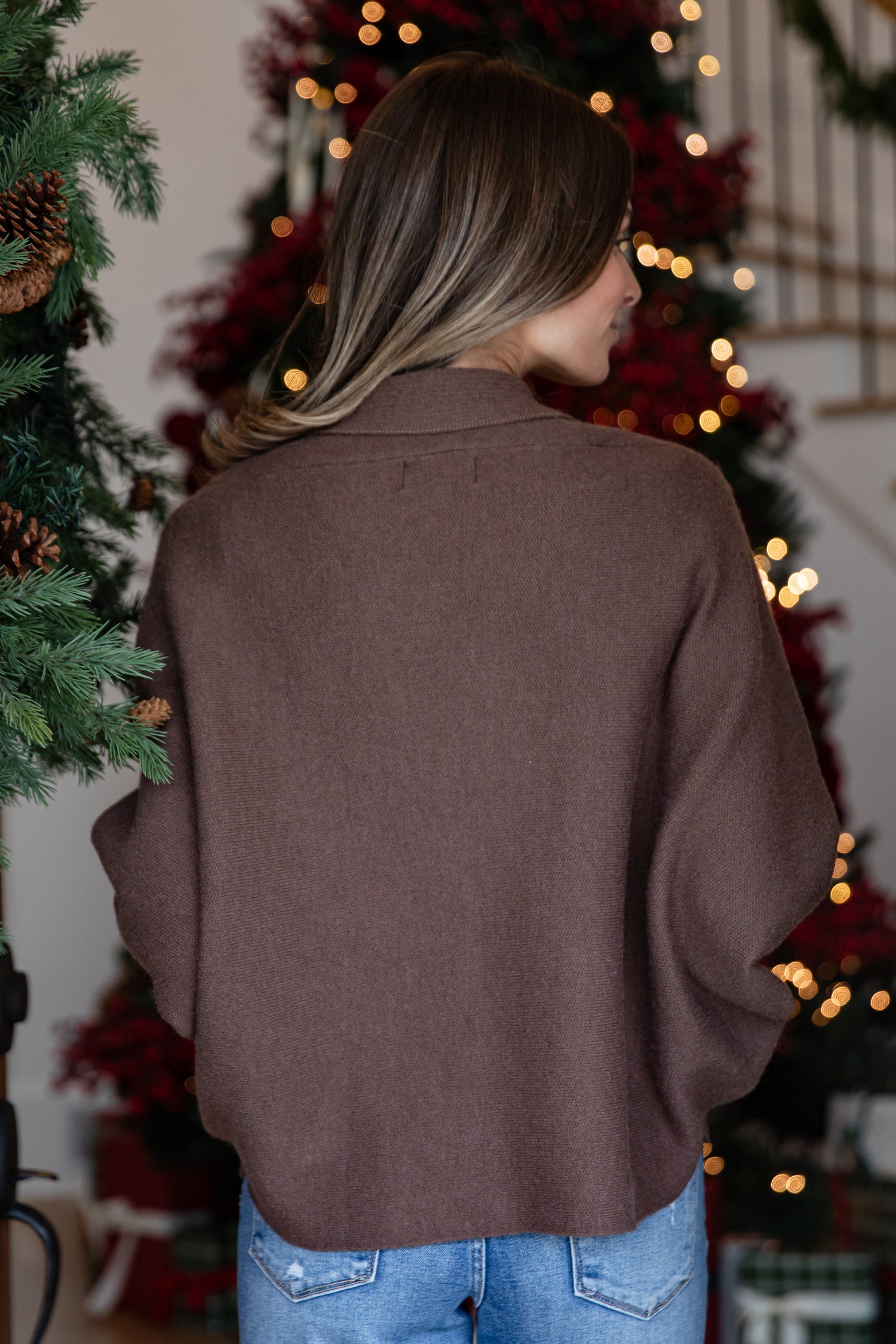 Person wearing a brown sweater in front of a decorated Christmas tree.