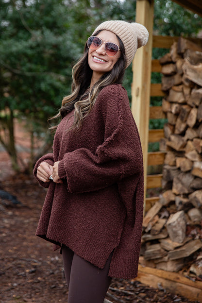 Woman wearing a brown sweater and beige beanie standing in front of stacked firewood.