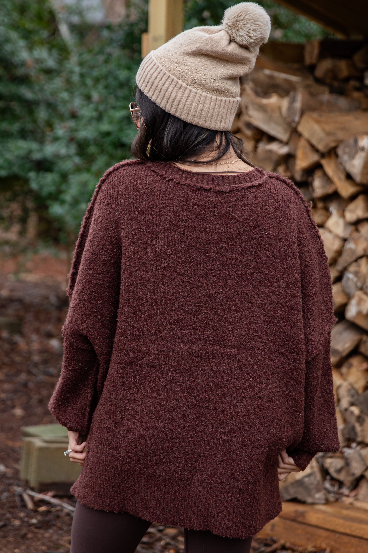 Person wearing a brown sweater and beige beanie in a forest setting