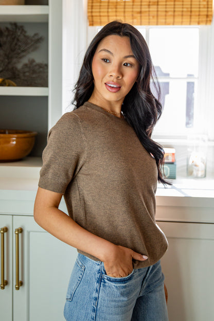 Woman wearing a brown shirt and blue jeans standing in a kitchen.