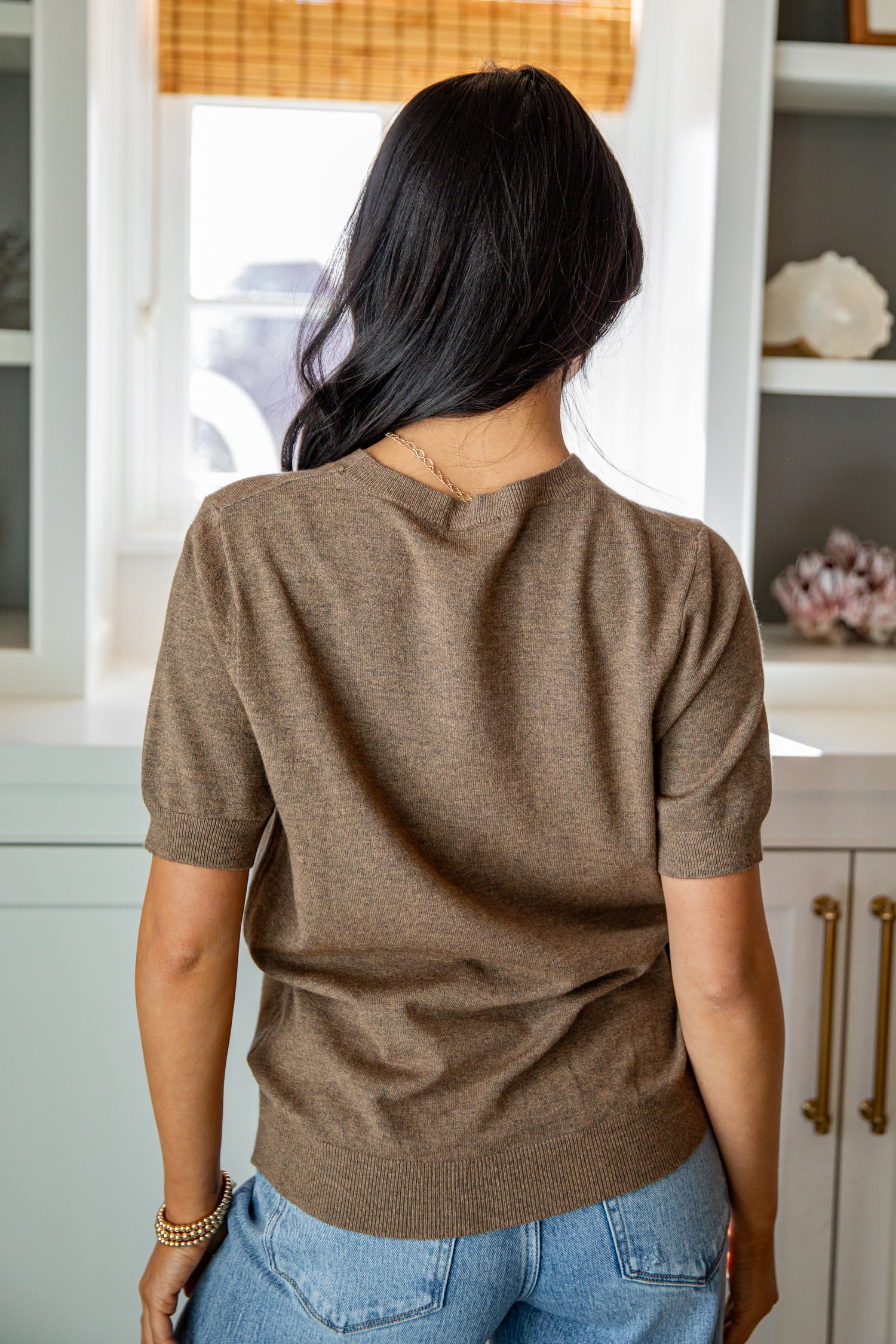 Person wearing a brown sweater and blue jeans in a kitchen setting