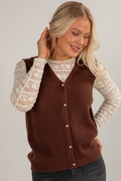 Woman wearing a brown button-up vest over a white lace top on a plain background