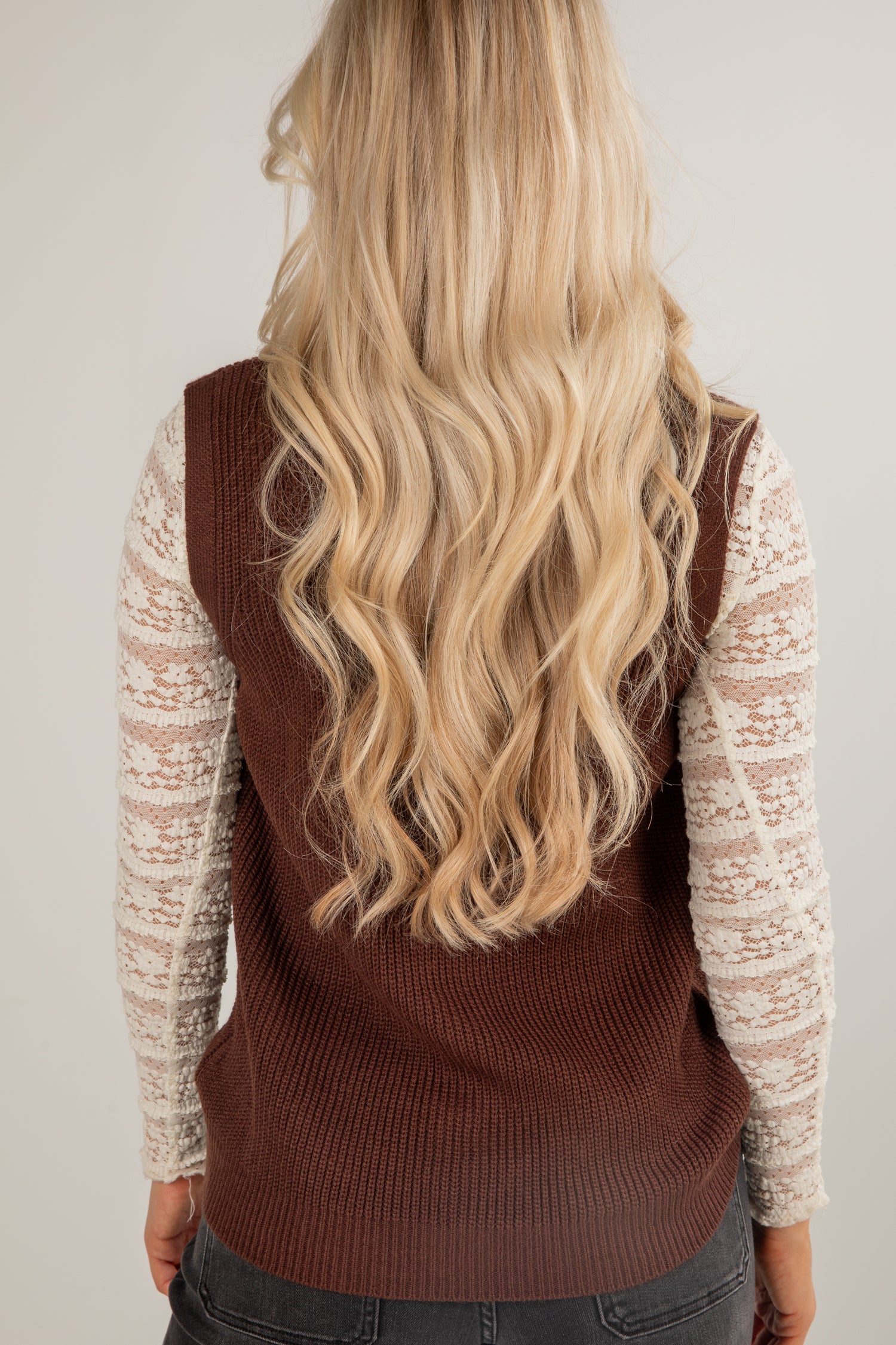 Person wearing a brown sweater vest over a light-colored long-sleeve shirt with blonde hair.