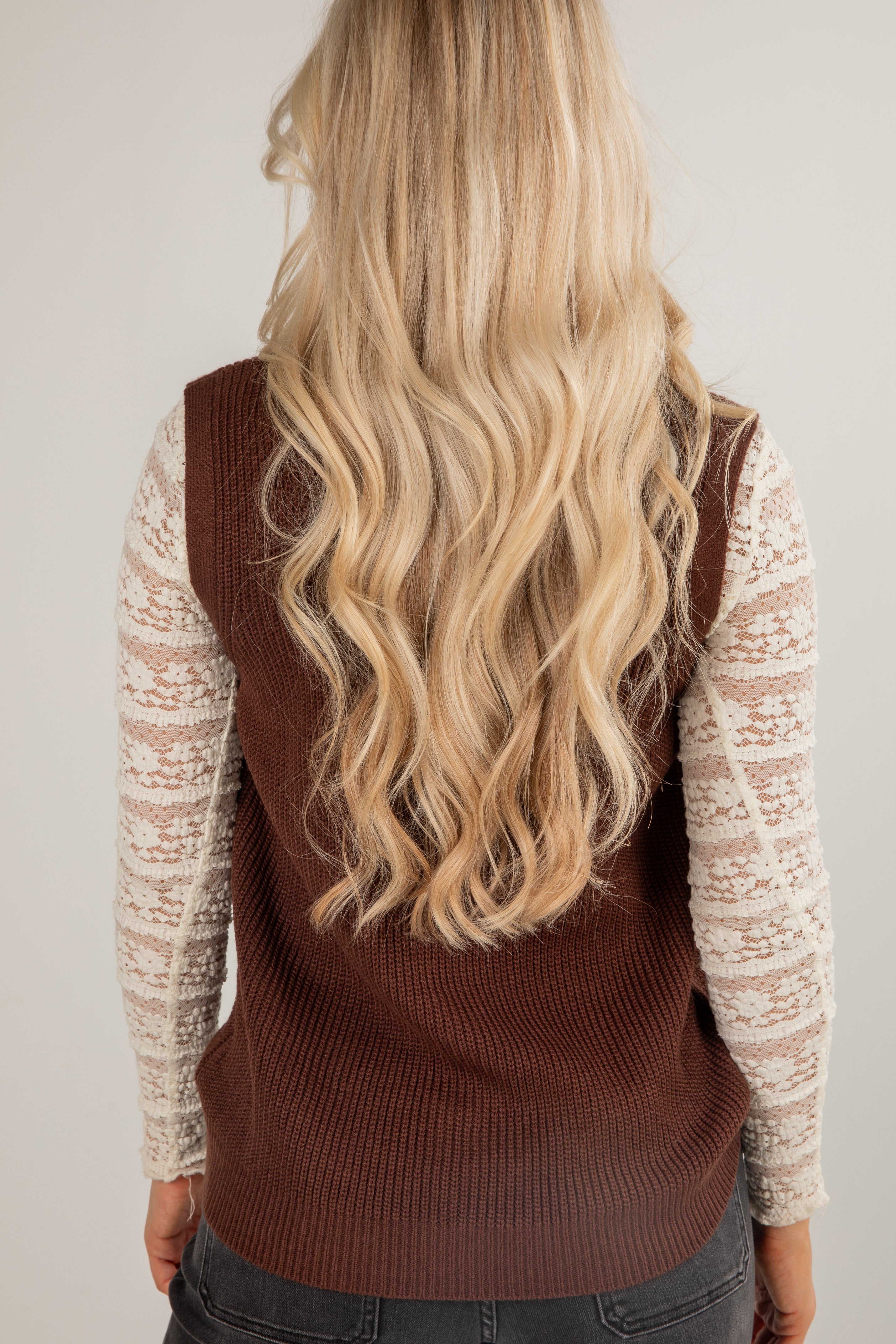 Person wearing a brown sweater vest over a light-colored long-sleeve shirt with blonde hair.