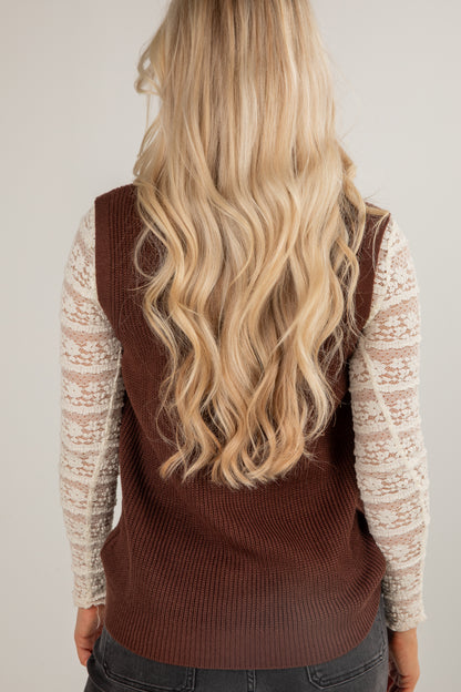 Person wearing a brown sweater vest over a light-colored long-sleeve shirt with blonde hair.