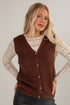 Woman wearing a brown knitted vest over a lace top against a plain background