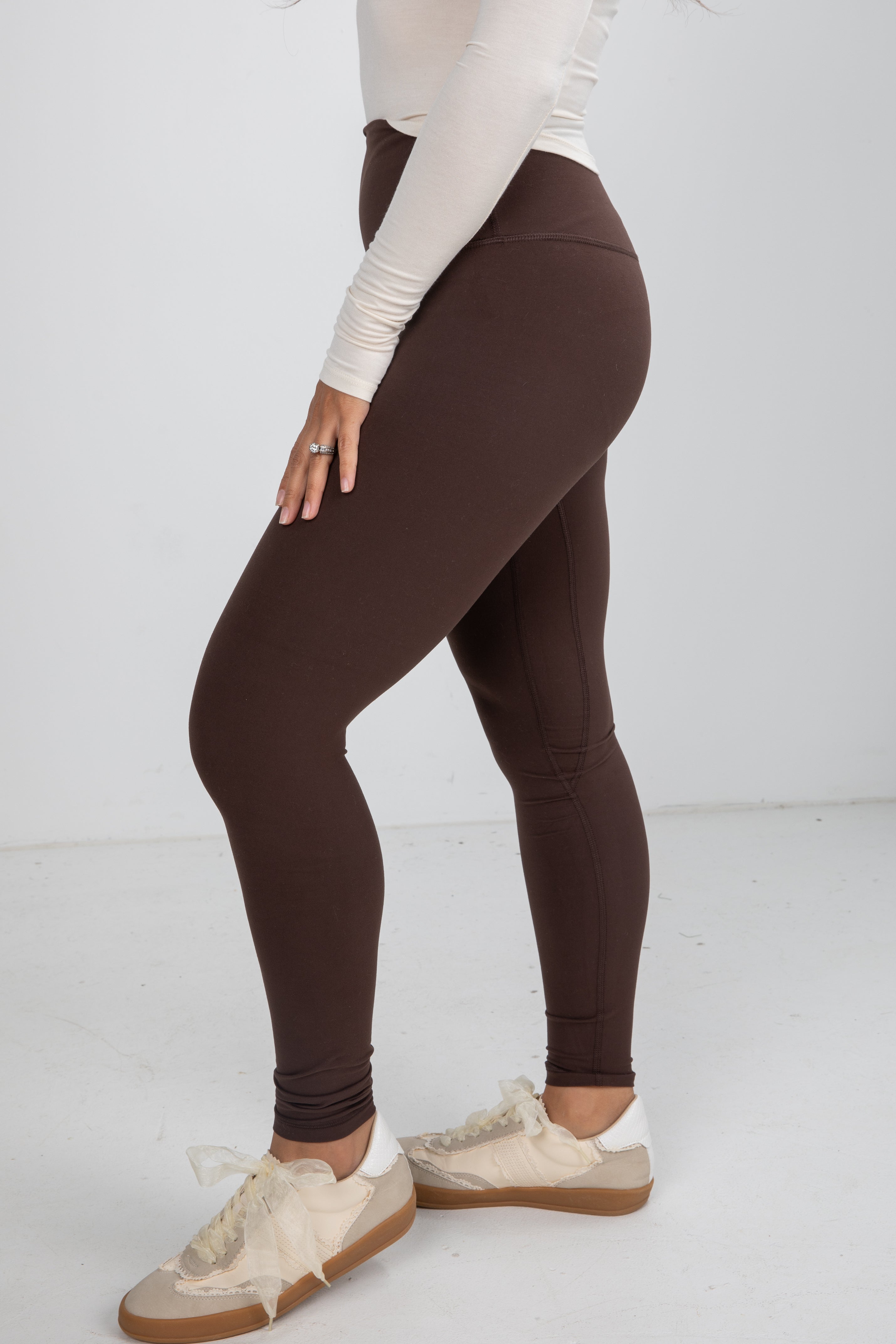 Person wearing brown leggings and white sneakers on a white background