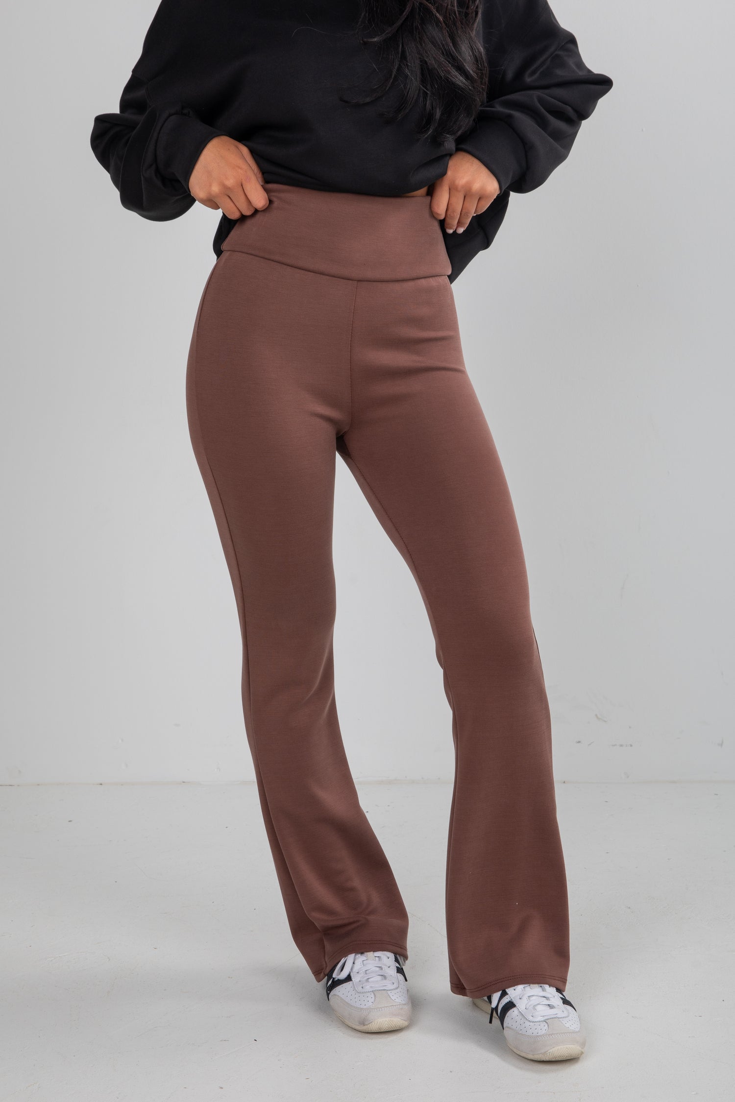 Person wearing brown pants and a black top on a white background